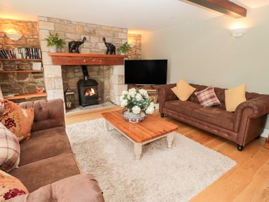 A living room with brown sofas a wooden coffee table with flowers a stone fireplace and a television at The Steadings in Rothbury