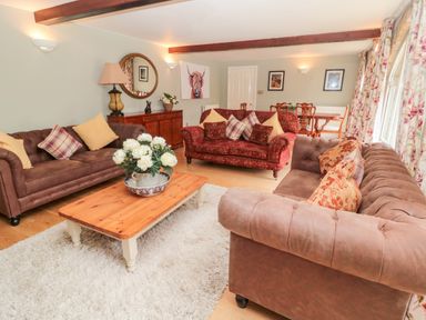 A living room with multiple sofas a wooden coffee table with flowers and a dining table in the background at The Steadings in Rothbury