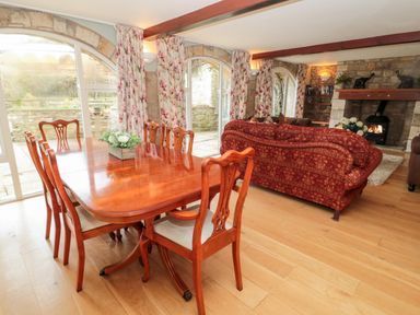 A dining room with wooden table and chairs next to a living room with red sofas and stone fireplace at The Steadings in Rothbury