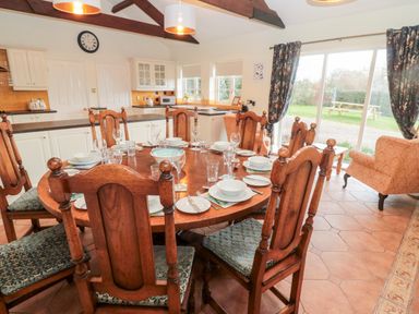 A dining area with a round wooden table set with plates and glasses and wooden chairs in a kitchen with white cabinets and a sliding glass door at The Steadings in Rothbury