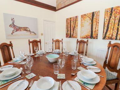 A dining room with a round wooden table set for eight with white bowls plates glasses and cutlery at The Steadings in Rothbury