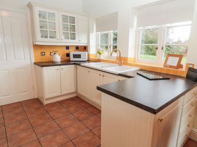 A kitchen with white cabinets a microwave kettle and sink by windows at The Steadings in Rothbury