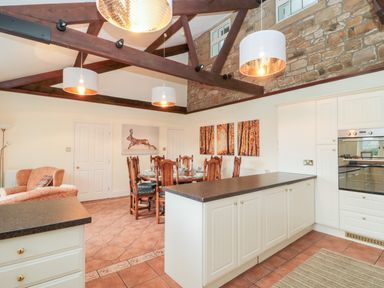 A kitchen and dining area with exposed beams stone wall and wooden dining chairs at The Steadings in Rothbury