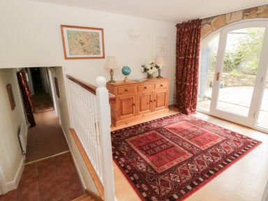 A hallway with wooden sideboard lamps globe and flowers next to glass doors with red curtains at The Steadings in Rothbury