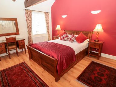A bedroom with a wooden bed and red bedding two bedside tables with lamps a wooden desk with chair and a mirror on the wall at The Steadings in Rothbury