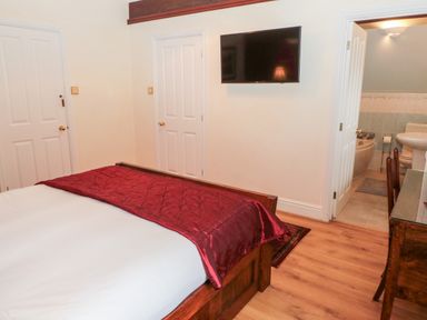 A bedroom with a wooden bed with white and red bedding a wall mounted television two closed doors and an open door leading to a bathroom at The Steadings in Rothbury