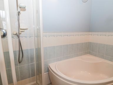 A bathroom with a corner bathtub and a shower with a handheld showerhead at The Steadings in Rothbury