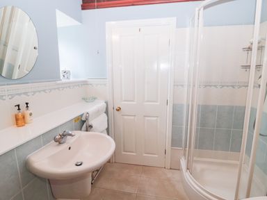 A bathroom with a wall-mounted sink round mirror towels on a rack and a corner shower enclosure at The Steadings in Rothbury