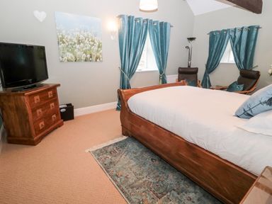 A bedroom with a wooden bed white bedding blue curtains a wooden chest of drawers and two armchairs at The Steadings in Rothbury