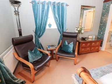 A seating area with two brown chairs and turquoise pillows by a window with turquoise curtains at The Steadings in Rothbury
