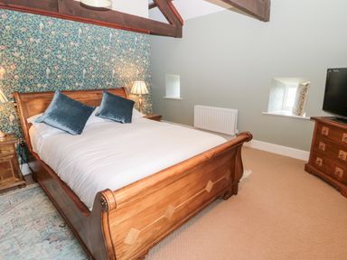A bedroom with a wooden bed with white bedding and blue pillows a wooden dresser with a television and wallpapered accent wall at The Steadings in Rothbury