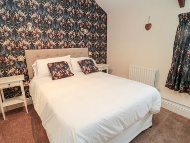 A bedroom with a double bed white bedding patterned pillows floral wallpaper and bedside tables at The Steadings in Rothbury