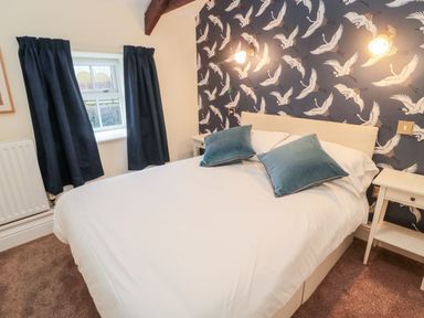A bedroom with a double bed two blue pillows nightstands and patterned wallpaper at The Steadings in Rothbury