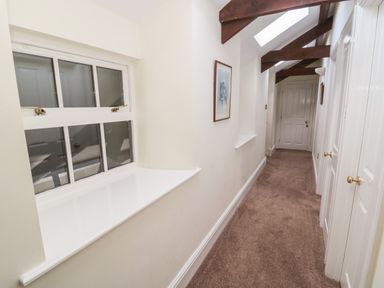 A narrow hallway with carpeted floor white walls wooden ceiling beams and a window at The Steadings in Rothbury