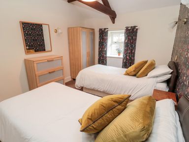 A bedroom with two single beds yellow pillows wooden dresser wardrobe and floral curtains at The Steadings in Rothbury