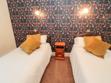 A bedroom with two single beds yellow pillows wooden nightstand and floral wallpaper at The Steadings in Rothbury