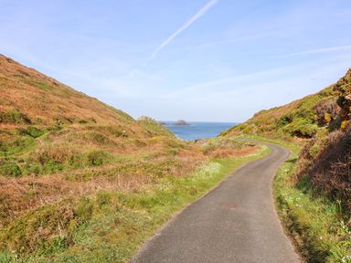 A winding road through hills with grass and shrubs leading to the sea at See Two Seas Cape Cornwall St Just