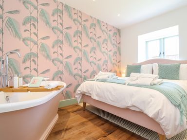 A bedroom with a bed and a bathtub next to a wall with patterned wallpaper at See Two Seas Cape Cornwall in St Just