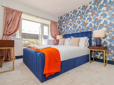 A bedroom with a blue bed frame white bedding orange throw pillows and an orange blanket with floral wallpaper and pink curtains at See Two Seas Cape Cornwall in St Just