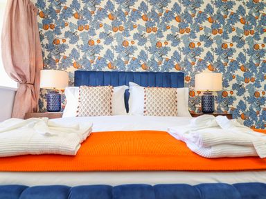 A bedroom with a blue upholstered bed headboard pillows bedside tables with lamps and patterned wallpaper at See Two Seas Cape Cornwall in St Just