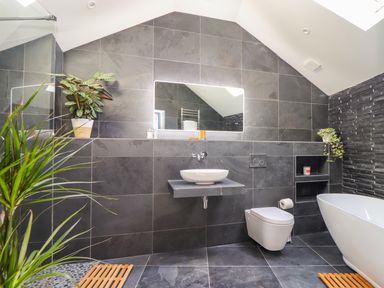 A bathroom with a wall-mounted sink, toilet, bathtub, plants, and a mirror at See Two Seas, Cape Cornwall in St Just
