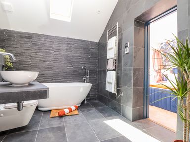 A bathroom with a freestanding bathtub a sink a toilet towel rack and tile walls and floor at See Two Seas Cape Cornwall in St Just