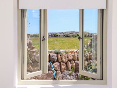 An open window showing a stone wall and a grassy field with houses in the distance at See Two Seas Cape Cornwall in St Just