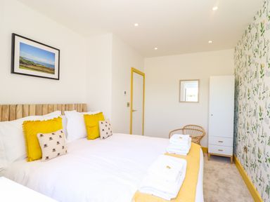 A bedroom with a bed white and yellow bedding a chair a wardrobe and floral wallpaper at See Two Seas Cape Cornwall in St Just