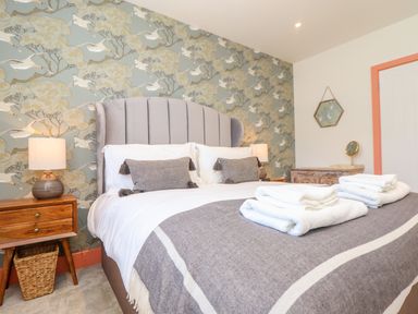 A bedroom with a bed with gray headboard and blankets bedside tables with lamps and a wicker basket at See Two Seas Cape Cornwall St Just