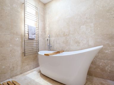 A bathroom with a white freestanding bathtub with a wooden bath tray and a metal towel rack with a towel at See Two Seas Cape Cornwall in St Just