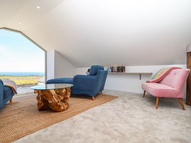 A living room with blue and pink chairs a wooden coffee table and a window with a view at See Two Seas Cape Cornwall