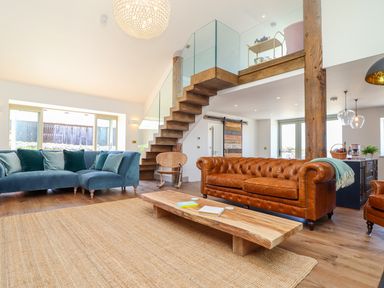 A living room with leather and fabric sofas wooden coffee table and staircase with glass railing at See Two Seas Cape Cornwall in St Just