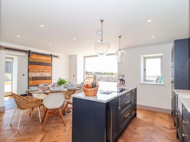 A kitchen and dining area with a wooden floor and blue cabinets at See Two Seas Cape Cornwall in St Just
