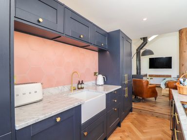 A kitchen with dark cabinets a marble countertop a white sink and pink hexagonal tile backsplash at See Two Seas Cape Cornwall in St Just