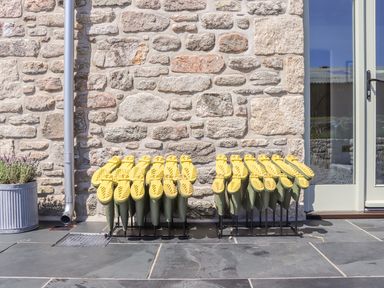 Two rows of yellow-soled green boots on racks outside a stone wall near a glass door at See Two Seas Cape Cornwall in St Just