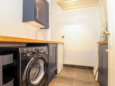 A laundry room with a washing machine wooden countertop and cabinets at See Two Seas Cape Cornwall in St Just