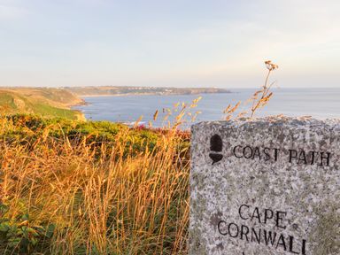 A coastal landscape with grass and cliffs overlooking the sea and a stone marker inscribed coast path cape cornwall at See Two Seas Cape Cornwall in St Just
