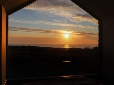 A sunset view of the ocean through a large triangular window at See Two Seas Cape Cornwall in St Just
