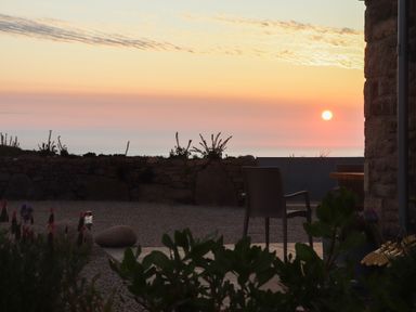 An outdoor patio area with chairs and plants facing a stone wall and a sunset at See Two Seas Cape Cornwall in St Just
