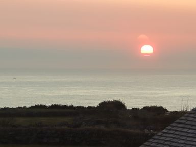 A sunset over the ocean with a small boat in the water and stone walls in the foreground at See Two Seas Cape Cornwall in St Just