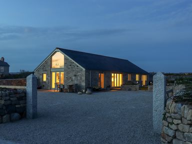 Stone house with lit windows and outdoor dining table on a gravel driveway at See Two Seas Cape Cornwall in St Just