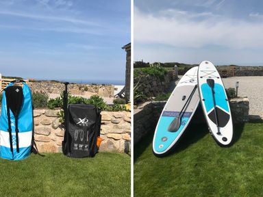 Two stand-up paddleboards with paddles on grass near stone walls and a house at See Two Seas Cape Cornwall in St Just