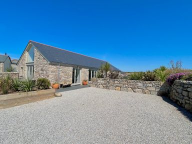 A stone house with slate roof and gravel driveway surrounded by stone walls and plants at See Two Seas Cape Cornwall in St Just