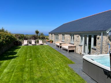 A grassy garden with lounge chairs stone house and a hot tub at See Two Seas Cape Cornwall in St Just