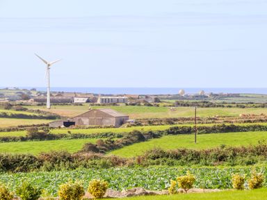 A rural landscape with green fields barns a wind turbine and a view of the sea at Pen Tewan in Sennen
