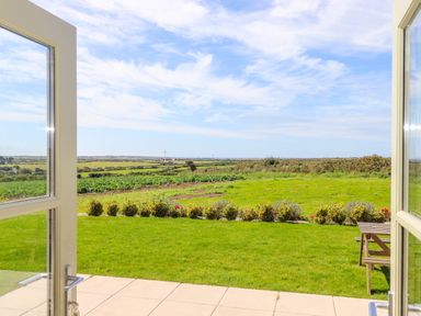 A garden with grass and a small hedge viewed through open doors at Pen Tewan in Sennen