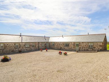 A stone cottage with multiple windows and doors on a gravel courtyard with flower pots at Pen Tewan in Sennen