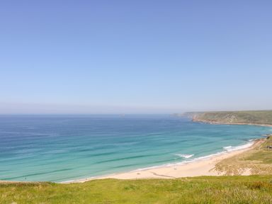 A coastal view with a sandy beach and grassy cliffs at Pen Tewan in Sennen