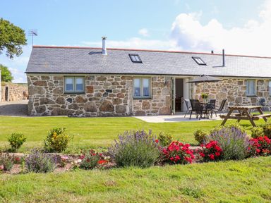 A stone cottage with a patio table and chairs an umbrella a picnic bench and a flower bed at Pen Tewan in Sennen