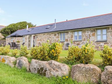 A stone cottage with several windows and a patio table with chairs and umbrella in a garden at Pen Tewan in Sennen